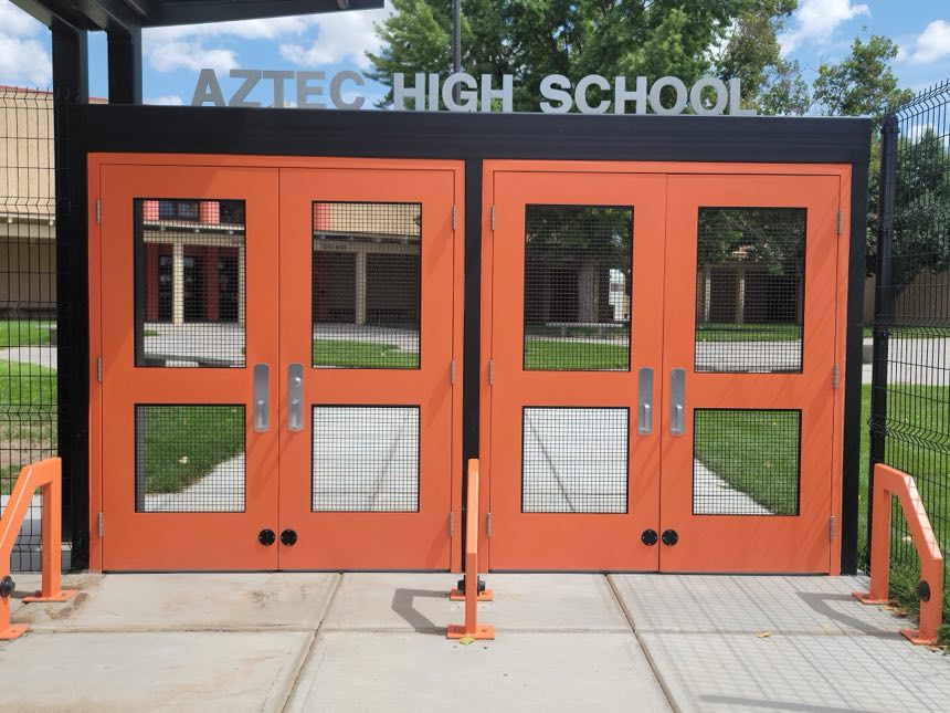 Two sets of orange commercial double doors with security mesh, installed at Aztec High School